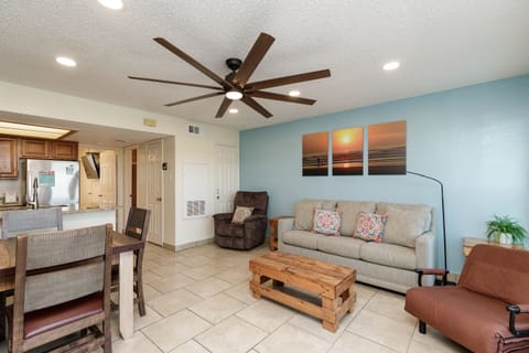 Relax in your bright, coastal-themed living room with comfortable seating, ocean artwork, and an open layout connecting to the kitchen.