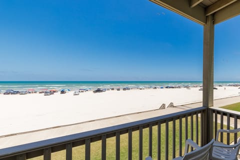 Expansive beach view from covered balcony overlooking pristine white sand, turquoise waters, and clear blue skies.