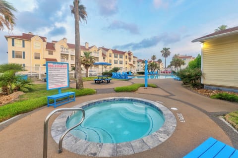 Resort complex features tropical landscaping with palm trees and colorful multi-story buildings surrounding the pool area.