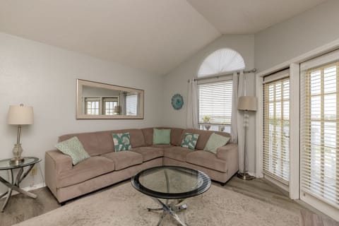 Sink into this cozy sectional sofa with tropical throw pillows, where natural light floods through elegant blinds and French doors.