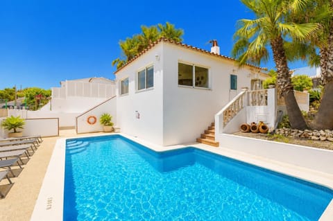 White villa featuring a private swimming pool, sun loungers, and tropical palm trees under a bright blue sky.