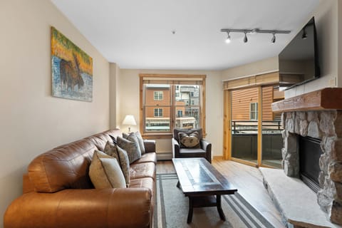 Unwind in your inviting living room, where a cozy leather sofa and stone fireplace set the scene for mountain evenings, and natural light pours in through large windows.