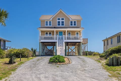 Coastal beach house elevated on stilts features wrap-around porch and convenient ground-level parking in scenic beachfront neighborhood.