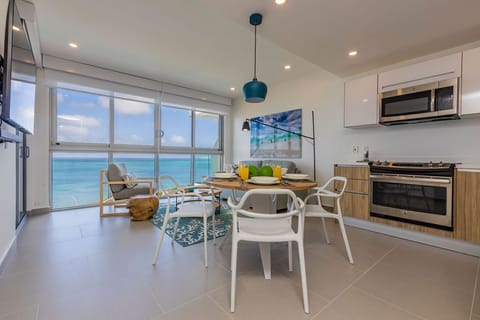 Picture yourself enjoying morning coffee at this bright dining table, surrounded by airy coastal style and stunning turquoise sea views through floor-to-ceiling windows.