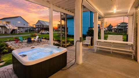 Private hot tub beneath the beach house with covered patio space, outdoor seating and a relaxing sunset setting.