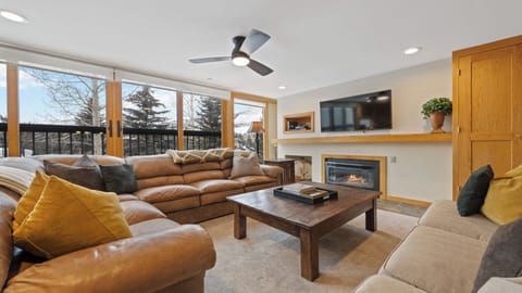 Unwind in your spacious living room with plush seating, a cozy fireplace, and sweeping views of towering pines through floor-to-ceiling windows.