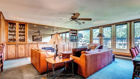 Relax in your spacious living room with plush leather sofas, warm wood accents, and expansive windows framing stunning mountain vistas—your perfect retreat awaits.