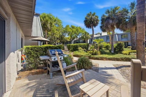 Stone pavers lead the way to this sun-drenched patio, where a gas grill and comfortable seating wait under the shade of tall palms. The lush greenery and blue sky create a peaceful outdoor kitchen perfect for bright afternoons.