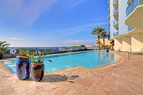Sparkling pool deck with decorative planters overlooking beachfront property grounds under clear blue skies.