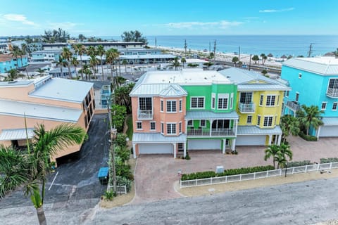 Aerial view of colorful beachside townhomes in a tropical coastal neighborhood, with palm trees lining the streets and pristine ocean waters just steps away.