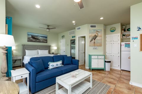 Relax in your coastal-themed studio with ocean artwork, plush blue sofa, and convenient kitchenette for your beach getaway.