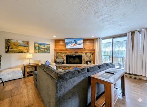 Unwind in your cozy living room with stone fireplace, mountain views, and plush seating perfect for après-ski relaxation.