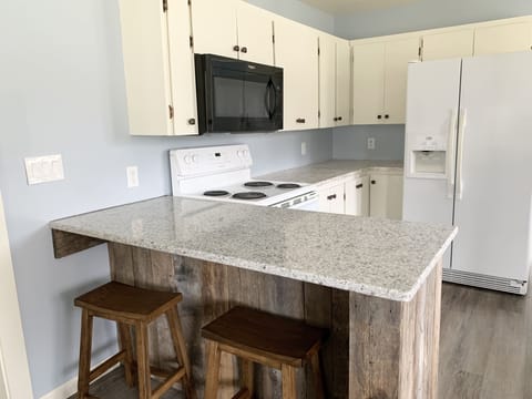 The kitchen features barstool seating, a oven/stove, microwave, and fridge.