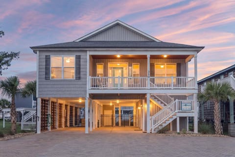 Beach house exterior with a lit porch and palms at Miles of Smiles, a 4-bedroom rental from Thomas Beach Vacations