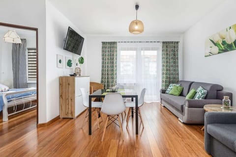 A bright and spacious living room featuring a dining table, chairs, and a cozy sofa with large windows allowing natural light.