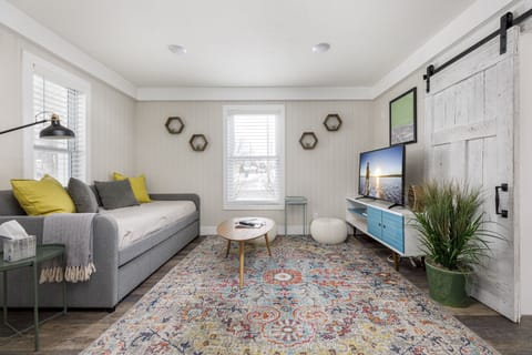 Bright living room w/ vaulted ceilings, plush sofa, colorful rug & wall-mounted TV for cozy movie nights.