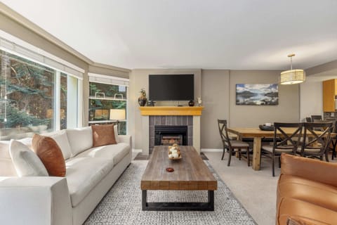 - Bright living room with forest views through wide windows  
- Cozy fireplace and TV for relaxing après-ski evenings  
- Open layout connects to dining area for easy gatherings  