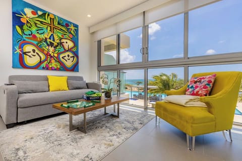 Unwind in your bright living space, where vibrant art and floor-to-ceiling windows frame stunning views of the pool and sparkling sea beyond.