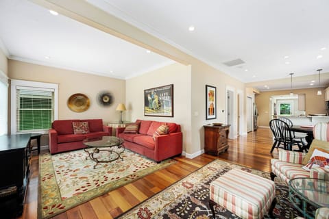 Relax in your stylish living room featuring warm hardwood floors, comfortable red sectional seating, and an open layout connecting to your fully equipped kitchen.