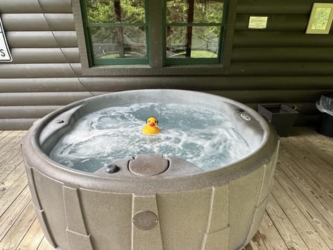 Outdoor hot tub bubbling with a yellow rubber duck, set on a wooden deck against dark log cabin walls.