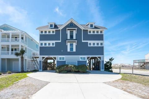 Beautiful Oak Island oceanfront home elevated on pilings with a circular driveway, covered parking, private beach access, and classic coastal architecture just steps from the Atlantic Ocean.