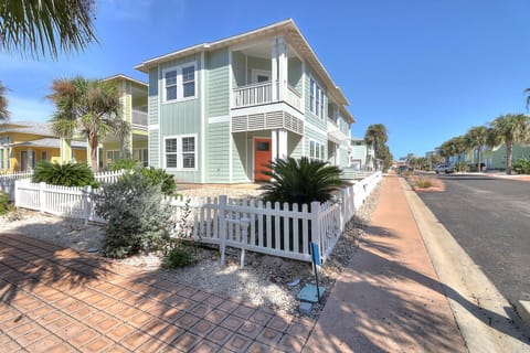 Charming two-story beach house with vibrant coral door and tropical landscaping in a peaceful coastal neighborhood.