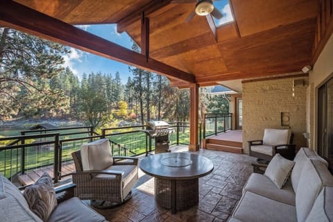 Large covered outdoor seating area with bbq, fire pit, and view of riverfront grassy backyard