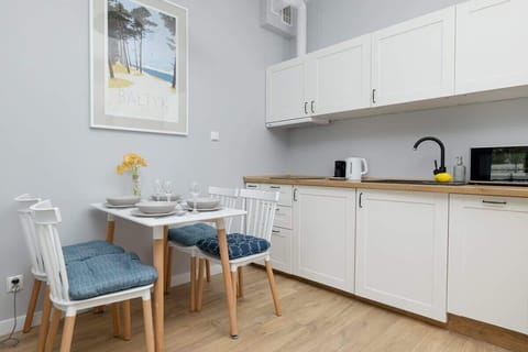 A compact dining area adjacent to a modern white kitchen, with soft wooden floors and minimalist decor.