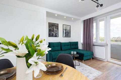 A spacious living room featuring a vibrant green corner sofa, a coffee table, and large windows allowing plenty of natural light.