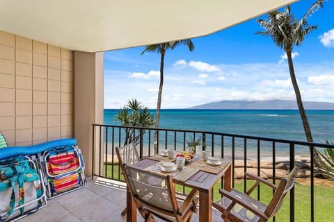 Balcony with dining table set for two, ocean horizon and palms stretching toward a distant island.