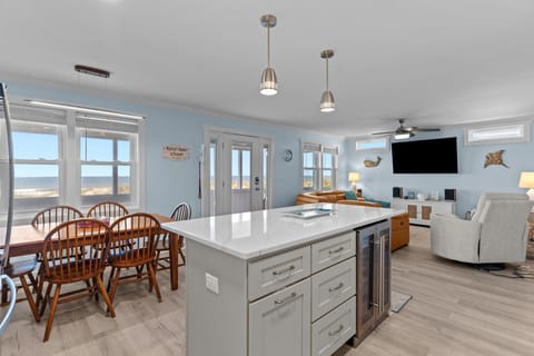 Bright kitchen with navy cabinets, white island, stainless appliances, pendant lights, marble counters, window over sink, pantry door, and coastal decor.