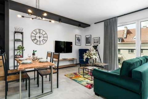  A stylish living room featuring a luxurious green velvet sofa, a coffee table with colorful decor, and a wall clock.