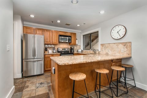Kitchen with stone countertops, stainless steel appliances, bar seating for four, and garage and laundry room access