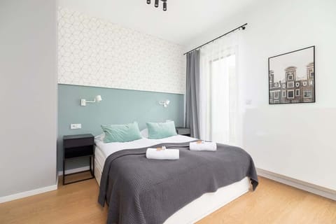 A modern bedroom with a double bed, gray bedding, and a mint-green accent wall, with a framed picture above the bed.