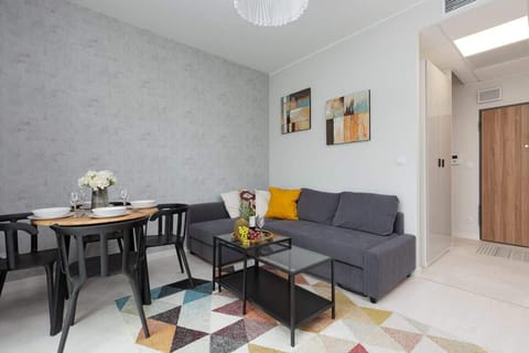 A cosy living room with a seating area combined with a dining area. A carpet in geometric shapes lies on the floor. Pictures hang on the wall.