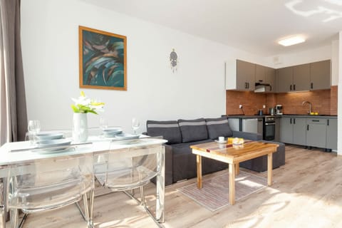 A modern living room with a gray sofa, a wooden coffee table, and a TV unit, connected to an open-plan kitchen.