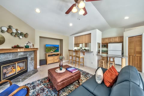 Stone fireplace lights the living room with a leather blue sofa, patterned rug, and wood bar stools by the kitchen counter.