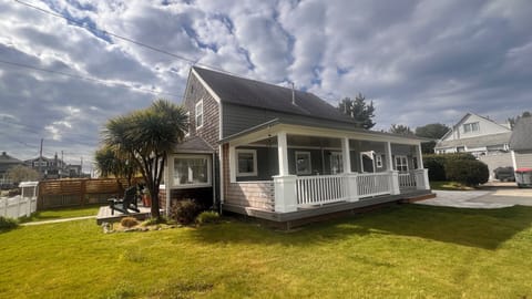 Charming coastal cottage with wraparound porch and lush lawn in peaceful residential neighborhood.