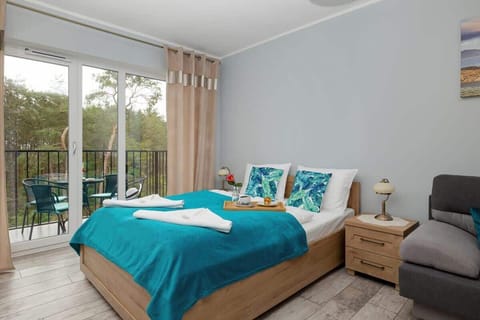 A bright studio apartment with a double bed, turquoise bedding, a sofa, and access to a balcony.