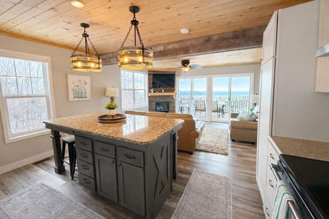 The updated kitchen opens seamlessly into the living room, featuring clean modern design, a TV, and ceiling fan. Sliding glass doors flood the space with light and lead to the deck, where Lake Superior views complete this bright, inviting gathering space.