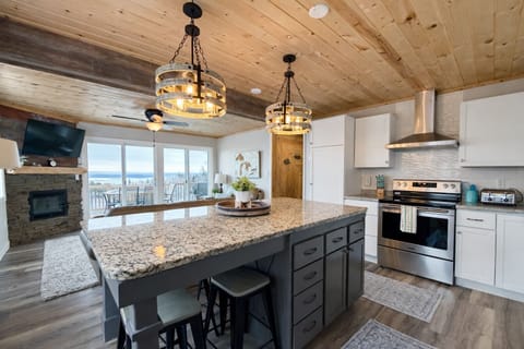 From the kitchen island, you overlook the living room with a fireplace, TV, and seating area. Through the deck doors, enjoy a Lake Superior view, plus the outdoor dining table and grill, perfect for a relaxing, scenic stay.