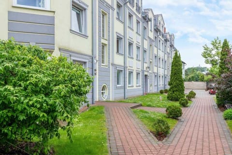 A lush green garden area with a paved pathway leading to the apartment building.