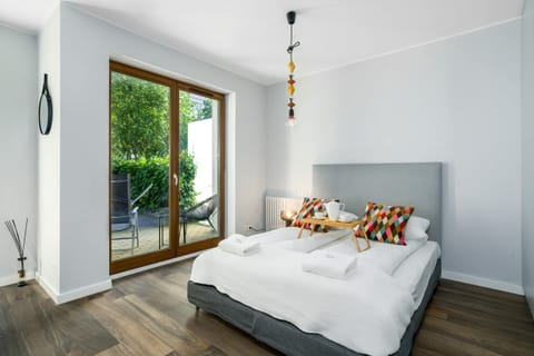 A cozy bedroom featuring a neatly made double bed with white linens, wooden flooring, and a modern lamp.