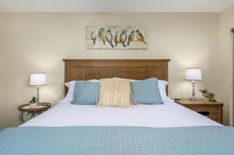 King bed with wooden headboard flanked by matching bedside tables, lamps, and bird-themed wall art.