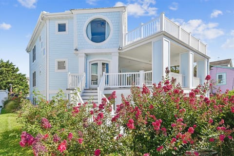 This charming coastal-inspired property features distinctive architectural details and inviting outdoor spaces surrounded by vibrant blooming gardens, creating a picturesque beach community setting.