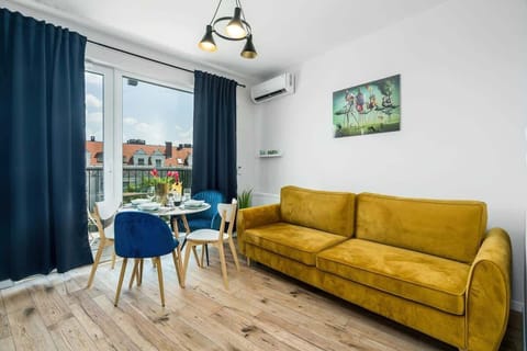 A stylish living room with a yellow sofa. The space is well-lit by natural light streaming through large windows with navy curtains.