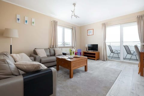 A spacious living room with a beige sectional sofa, wooden coffee table, and light walls, creating a cozy and welcoming atmosphere.
