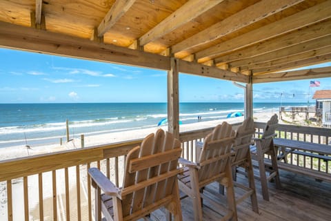 Covered oceanfront deck with Adirondack chairs overlooking the beach and waves—perfect for relaxing, dining, and enjoying stunning Oak Island, NC coastal views.