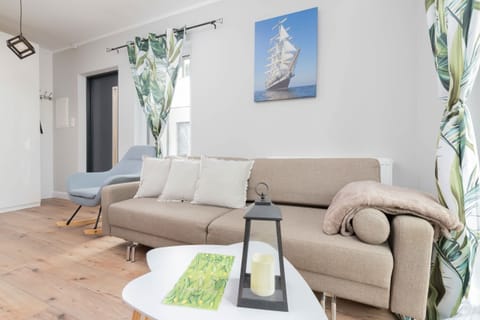 A bright living room with a light beige sofa, a coffee table, and a colorful wall painting above the couch. The decor is minimalist with natural light streaming in.