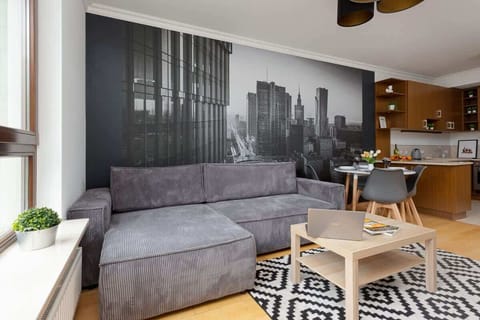 A cozy living room with a gray sofa, a wooden coffee table, and a monochrome cityscape wall mural. The decor is modern with a geometric rug.